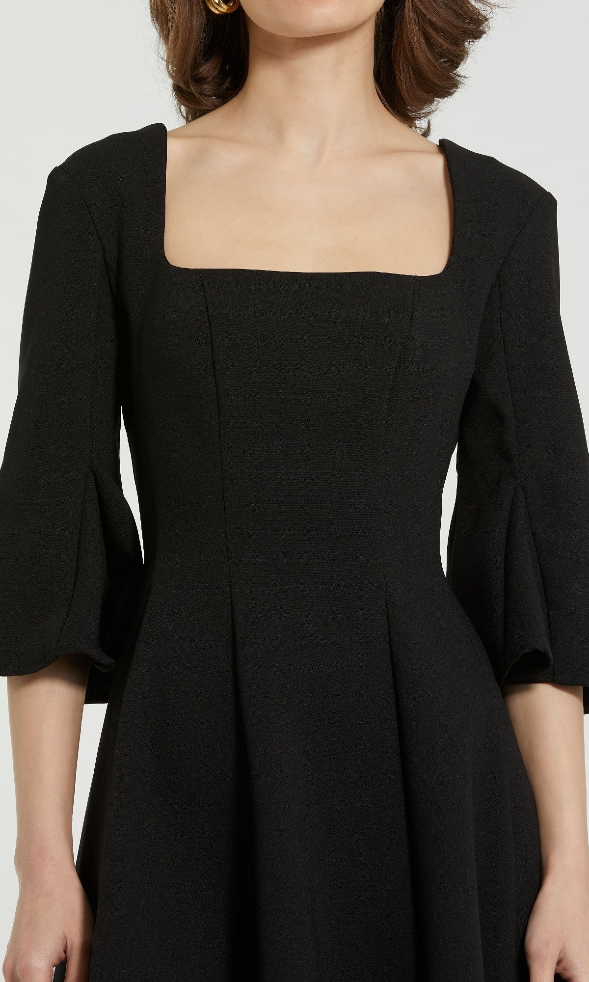 A woman stands against a plain background wearing the Mac Duggal 21011 Cute Short Black Party Dress, featuring a square neckline and three-quarter sleeves.